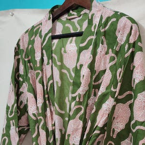 May include: Green robe with a repeating pattern of pink tigers. The robe has long sleeves and a matching tie belt. The trim is white. The robe is hanging on a wooden hanger.