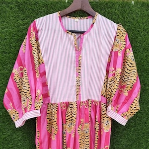May include: A pink and white striped dress with a tiger print. The dress has a collared neckline, long sleeves, and a gathered waist. The sleeves and skirt feature a tiger print, while the bodice is striped.