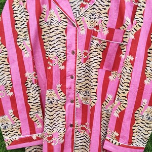 May include: Pink and red striped pajama set with a tiger print. The long-sleeved top has a collared neckline, a chest pocket, and button closures. White trim accents the collar, cuffs, and pocket. The pajama set is made of a soft fabric.