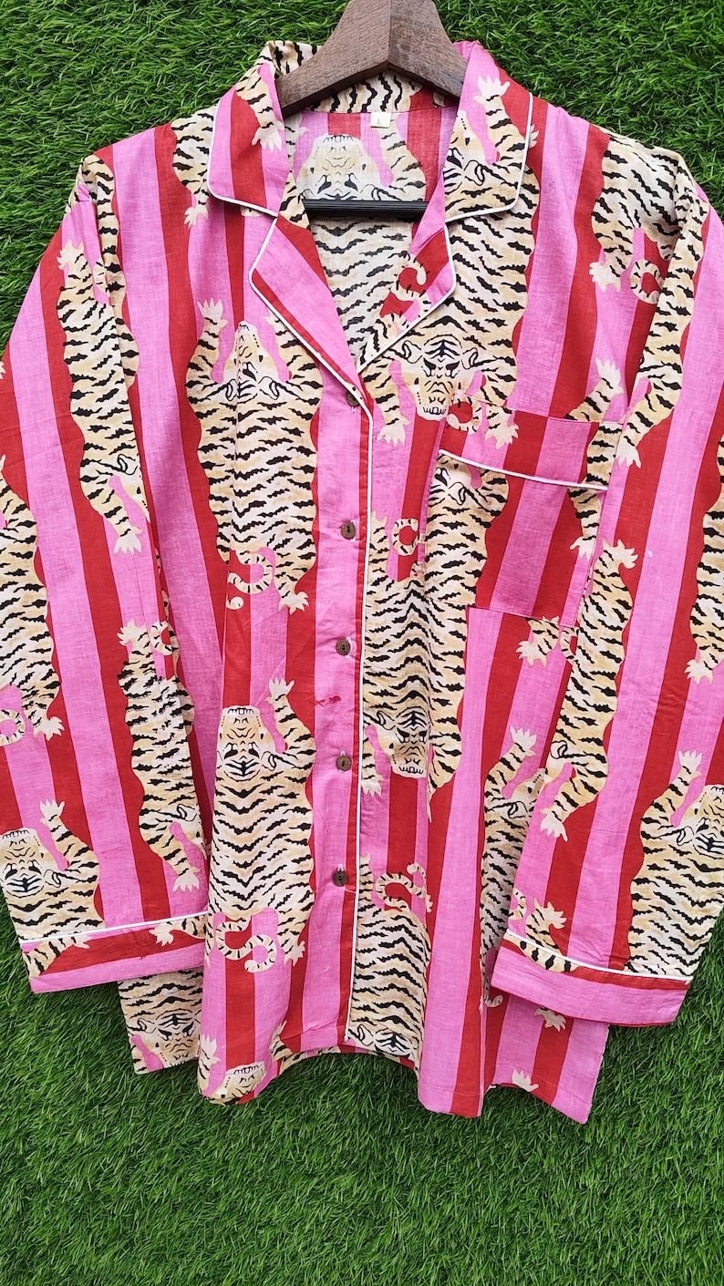 May include: Pink and red striped pajama set with a tiger print. The long-sleeved top has a collared neckline, a chest pocket, and button closures. White trim accents the collar, cuffs, and pocket. The pajama set is made of a soft fabric.