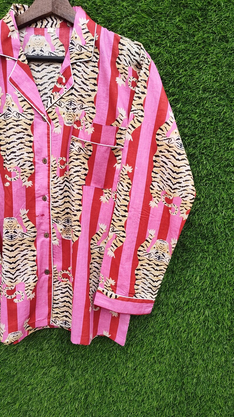 May include: Pink and red striped pajama top with a tiger print. The long-sleeved top has a button-down front, a chest pocket, and white trim. The tiger print features tan and black stripes.