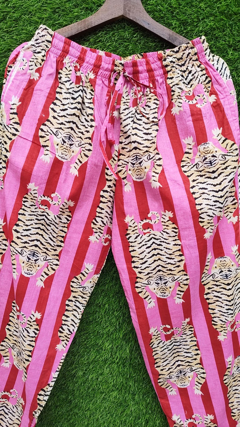 May include: Pink and red striped pajama pants with a repeating tiger print. The pants have a drawstring waist and a relaxed fit. The tigers are tan with black stripes.