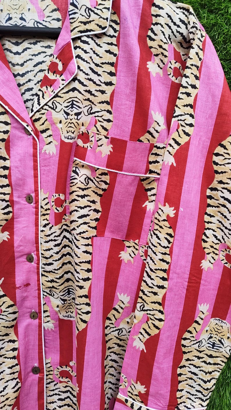 May include: Pink and red striped pajama shirt with a tiger print. The shirt has a button-down front, a chest pocket, and white trim. The tiger print features tan and black stripes.