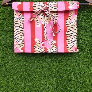 May include: Pink and red striped fabric with a tiger print, folded and tied with a matching ribbon. The fabric is hanging on a wooden hanger against a green background. The tiger print features black and tan stripes.