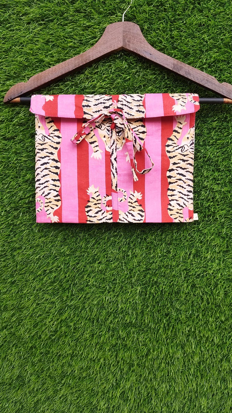 May include: Pink and red striped fabric with a tiger print, folded and tied with a matching ribbon. The fabric is hanging on a wooden hanger against a green background. The tiger print features black and tan stripes.