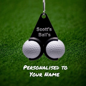 Könnte beinhalten: Schwarzer Golfballhalter mit zwei Golfbällen. Der Halter hat ein schwarzes Dreieck mit dem Text "Scott's Ball's" und dem Text "Personalisiert mit Ihrem Namen" unter dem Halter.