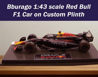 May include: A 1:43 scale model of a Red Bull F1 car on a custom plinth. The car is predominantly black with red and yellow accents, and sponsor logos. The plinth is black and displays the Oracle Red Bull Racing logo. The text "Bburago 1:43 scale Red Bull F1 Car on Custom Plinth" is visible.
