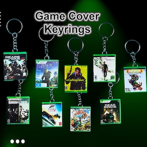 May include: A set of ten video game keyrings featuring different game covers. The keyrings are made of metal and have a clear plastic cover over the game artwork. The game titles include "Gears of War", "Halo Infinite", "Cyberpunk 2077", "Quantum Break", "Dead Space", "Forza Horizon 5", "Rainbow Six Siege", "Ghost of Tsushima", "Rare Replay", and "The Last of Us Part II".
