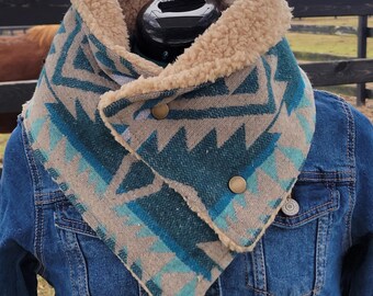 Könnte beinhalten: Ein Halswärmer im Südwest-Stil mit einem geometrischen Muster in Türkis, Grau und Beige. Der Halswärmer hat ein weiches, hellbraunes Futter und wird mit zwei großen, runden Knöpfen befestigt. Er wird über einer Jeansjacke getragen.