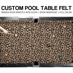 May include: A custom pool table felt with a leopard print design. The felt is brown and tan with black pockets and a silver frame. The text "CUSTOM POOL TABLE FELT" is at the top of the image. The image also states "IMAGES DYED DIRECTLY INTO CLOTH | STAIN RESISTANT | FULL COLOR".