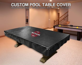 May include: A black custom pool table cover with the text "Fire Matthews Dept" in red and white. The cover is on a wooden pool table in a room with a second table and stairs.