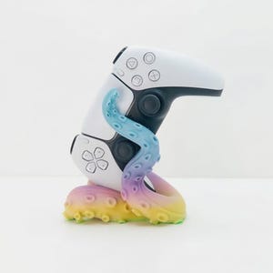 May include: A white and black game controller with a colorful octopus design. The octopus tentacles are blue, purple, pink, and yellow. The controller has a flower-shaped button and other circular buttons.