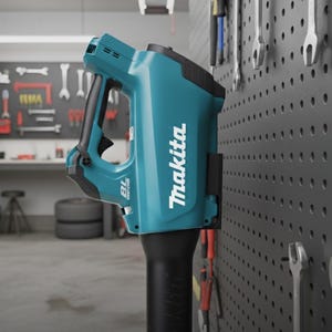 Puede incluir: Una herramienta eléctrica Makita turquesa y negra está montada en un panel perforado gris en un taller. La herramienta tiene un mango negro y el logotipo de Makita en blanco. Llaves y otras herramientas cuelgan del panel perforado.