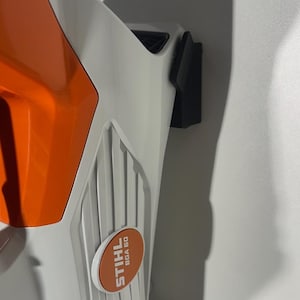 Può includere: Un soffiatore senza fili STIHL BGA 60 bianco e arancione. Il soffiatore ha un design curvo con un corpo bianco e dettagli arancioni. Il logo STIHL e il modello BGA 60 sono visibili su un adesivo arancione e bianco.