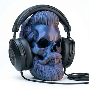 May include: A decorative skull with a beard and hair, painted in shades of blue and purple, wearing black headphones. The headphones have a skull logo on the earcups and a black cable.
