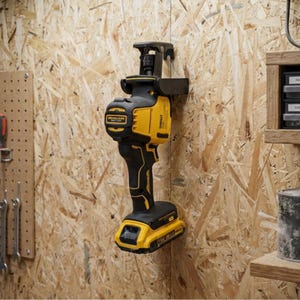 Puede incluir: Una sierra recíproca inalámbrica de color amarillo y negro montada en un soporte de pared negro. La herramienta eléctrica cuenta con una carcasa de motor sin escobillas, una batería en la base y una abrazadera de hoja de metal en la parte superior.