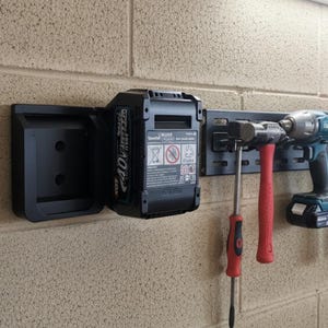 May include: Black wall-mounted tool organizer with a 40V battery, hammer, drill, and various screwdrivers. The tools are neatly arranged on a black metal rail, providing a practical storage solution for a workshop or garage.