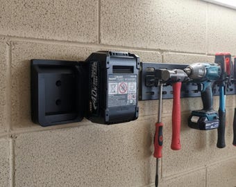 Può includere: Organizzatore di utensili nero da parete con batteria da 40V, martello, trapano e vari cacciaviti. Gli utensili sono ordinatamente disposti su una guida metallica nera, offrendo una soluzione di stoccaggio pratica per un'officina o un garage.