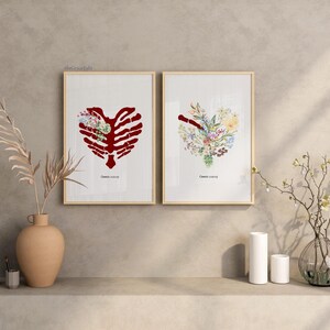 K&ouml;nnte beinhalten: Zwei gerahmte Kunstdrucke. Einer zeigt einen roten Brustkorb in Herzform mit floralen Akzenten. Der andere Druck hat ein herzf&ouml;rmiges Blumenarrangement. Beide Drucke haben einen hellen Holzrahmen und stehen auf einem Regal.