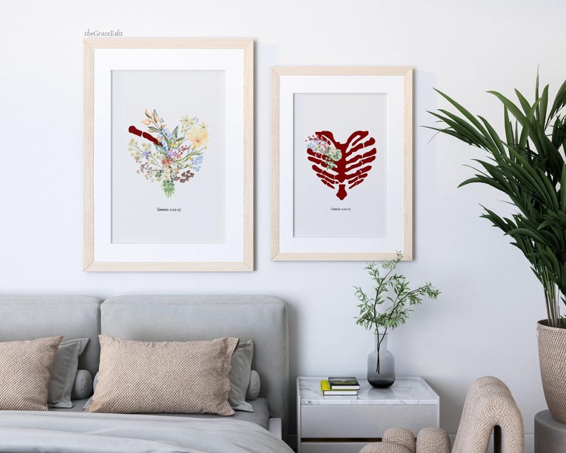 K&ouml;nnte beinhalten: Zwei gerahmte Kunstdrucke. Einer zeigt eine Herzform aus bunten Blumen, der andere ein rotes Rippenherz mit Blumen. Beide sind in hellen Holzrahmen und haben unten Text. Die Drucke werden &uuml;ber einem Bett ausgestellt.