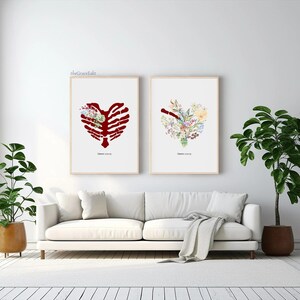 K&ouml;nnte beinhalten: Zwei gerahmte Kunstdrucke mit herzf&ouml;rmigen Designs. Einer zeigt einen roten Brustkorb, der andere ein Blumenarrangement. Beide sind vor einem wei&szlig;en Hintergrund, mit Text unten. Die Rahmen sind hell, und die Kunst h&auml;ngt &uuml;ber einem wei&szlig;en Sofa.