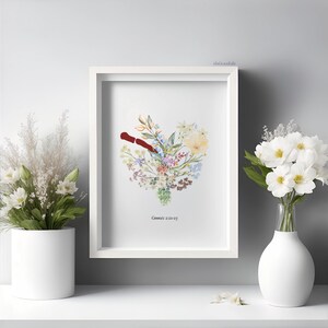 K&ouml;nnte beinhalten: Ein gerahmter Kunstdruck mit floralem Motiv, der eine herzf&ouml;rmige Anordnung aus bunten Blumen und Gr&uuml;n zeigt. Ein rotes Element befindet sich in der Mitte des Herzens. Der Text "Genesis 2:21-25" steht unten. Wei&szlig;e Vase mit wei&szlig;en Blumen.