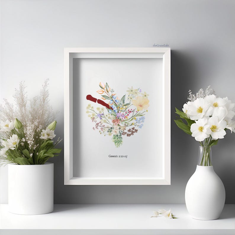 K&ouml;nnte beinhalten: Ein gerahmter Kunstdruck mit floralem Motiv, der eine herzf&ouml;rmige Anordnung aus bunten Blumen und Gr&uuml;n zeigt. Ein rotes Element befindet sich in der Mitte des Herzens. Der Text "Genesis 2:21-25" steht unten. Wei&szlig;e Vase mit wei&szlig;en Blumen.