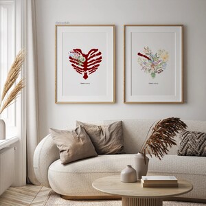 K&ouml;nnte beinhalten: Zwei gerahmte Kunstdrucke mit herzf&ouml;rmigen Designs. Eines zeigt einen roten Brustkorb, gef&uuml;llt mit Blumen, das andere ein Blumenherz. Beide befinden sich in goldenen Rahmen und h&auml;ngen &uuml;ber einem beigen Sofa.