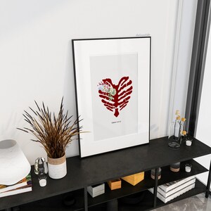 K&ouml;nnte beinhalten: Gerahmter Kunstdruck mit einem roten Brustkorb-Herz-Design und einem Blumenarrangement in der Mitte. Das Kunstwerk wird in einem schwarzen Rahmen vor einem wei&szlig;en Hintergrund pr&auml;sentiert. Der Text "Genesis 2:23-25" befindet sich unten.