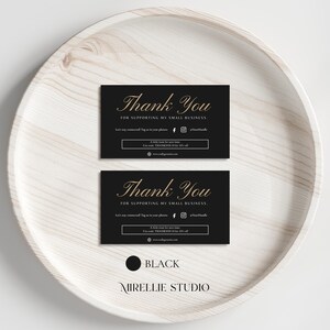 Puede incluir: Dos tarjetas de agradecimiento negras con letras doradas que dicen "Thank You For Supporting My Small Business". Las tarjetas incluyen iconos de redes sociales y una dirección web. Están sobre una bandeja de madera blanca.