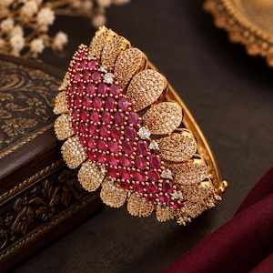 Peut inclure: Un bracelet jonc articulé doré présentant un motif en éventail semi-circulaire. La pièce centrale est ornée de nombreuses pierres roses vibrantes de taille ovale et de petits cristaux clairs pavés disposés en pétales texturés.