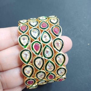 May include: Four gold bangles with green and white enamel and red and white stones.