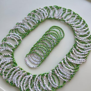 May include: A collection of numerous circular bracelets made from small green seed beads. Each bracelet features white letter beads spelling out I HEART PICKLES, with a small red heart symbol replacing the word heart in the text sequence.