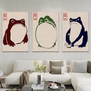 Puede incluir: Tres impresiones enmarcadas de ranas en diferentes colores. La primera rana es roja, la segunda rana es verde y la tercera rana es azul. Cada rana está sentada sobre un fondo blanco con un sello rojo que dice "青" en japonés.