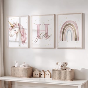 May include: Three framed prints for wall art. One shows a unicorn with a pink mane and golden horn. The second has the letter "H" and the name "Halley" in pink script. The third print depicts a rainbow in muted tones. Baskets and toy houses are on a white shelf.