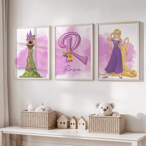 May include: Three framed prints featuring a purple and green tower, a purple letter R with the name Rosa, and a cartoon of Rapunzel with long blonde hair. The prints are hanging on a white wall above a white shelf with two wicker baskets and two small wooden houses.