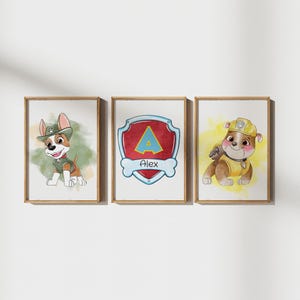 May include: Three framed watercolor prints featuring cartoon puppies. One puppy wears a green hat and vest, another has a shield with the name "Alex", and the third wears a yellow construction hat and vest. The prints are in wooden frames.
