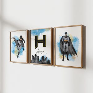 May include: Three framed Batman art prints. The prints feature Batman in various poses, with watercolor backgrounds in blue and yellow. One print includes the name "Hugo" and a cityscape.