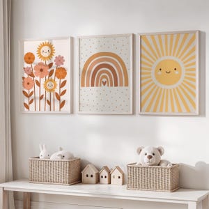 Può includere: Tre stampe artistiche incorniciate con un tema allegro. Una stampa mostra girasoli sorridenti, un'altra un arcobaleno con un cuore e la terza un sole sorridente con raggi. Le stampe sono esposte sopra cesti intrecciati e casette di legno.