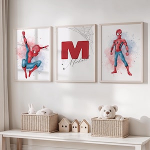 May include: Three framed watercolour prints featuring Spider-Man. One shows Spider-Man swinging, another has a large red "M" with "Michael" below, and the third depicts Spider-Man standing. The prints have a light wood frame.