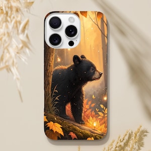 May include: A phone case featuring a black bear cub in a forest scene with autumn leaves and warm lighting. The case has a glossy finish and a detailed illustration of the bear and its surroundings.