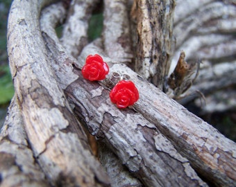 May include: A pair of red rose-shaped earrings with silver posts. The earrings are displayed on a piece of weathered wood.
