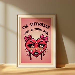 Puede incluir: Impresión artística enmarcada con una cara en forma de corazón, adornada con lazos y lágrimas, sobre un fondo rosa. El texto "I'm Literally Just a Punk Girl" se muestra encima del corazón. La obra está en un marco de madera.