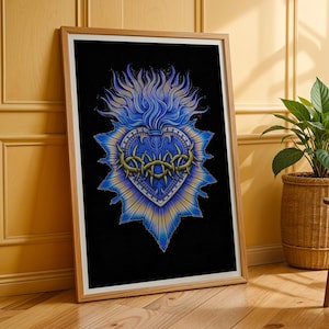 Puede incluir: Impresión artística enmarcada con un diseño de Sagrado Corazón azul y amarillo sobre fondo negro. El corazón está adornado con una corona de espinas y llamas. La obra de arte se muestra en un marco de madera, apoyada en una pared.