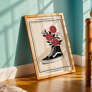 Puede incluir: Una impresión artística enmarcada que presenta una zapatilla alta en blanco y negro con flores rojas y hojas verdes. La obra de arte está sobre un fondo crema con un borde negro y se muestra en un marco de madera.