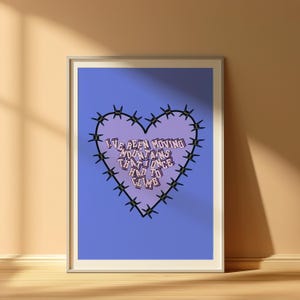 Puede incluir: Impresión artística enmarcada con un fondo azul y un diseño en forma de corazón. El corazón está delineado con alambre de púas y contiene el texto "We Been Moving Mountains That Once Had To Climb" en una fuente estilizada.