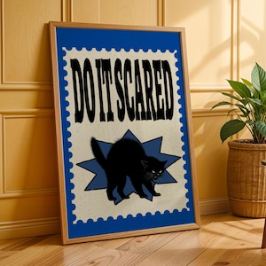Può includere: Un poster rettangolare incorniciato con un bordo blu dai bordi smerlati. Il centro mostra il testo DO IT SCARED in grassetto nero sopra una sagoma nera di un gatto con la schiena arcuata posizionato su una forma di stella blu.