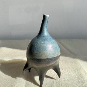 May include: A blue and black ceramic vase with a unique, rounded shape and three legs.