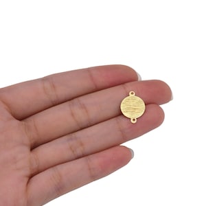 May include: Gold-toned metal circle charm with two jump rings. The circle has a textured surface.