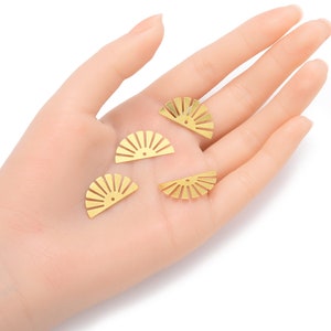 May include: Four gold-colored metal sunburst shapes with a hole in the center. The shapes are arranged on a hand.